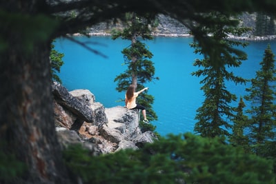 女孩坐在悬崖上，靠近树木，指向水体